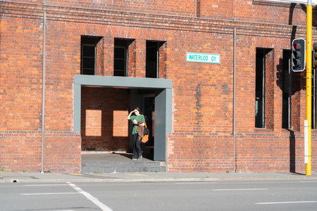 Wellington New Zealand - July 31 2021; Woman in green top shield eyes from sun as she enters gallery opening into street of heritage wool shed known as Shed 21 on Waterloo Quay, Wellingtonのeditorial素材