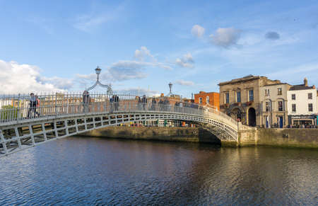 Dublin Ireland - August 16 2017; People crossing on the pedestrian Ha'penny Bridge across Liffey River in city in late afternoon light.のeditorial素材