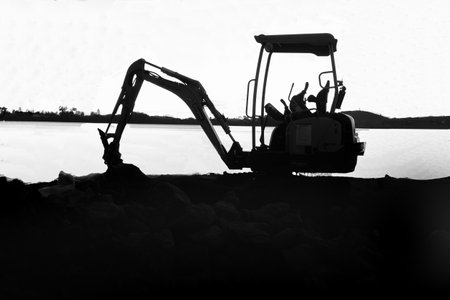Earth digger standing idle in silhouette on waters edge with land on horizonの写真素材