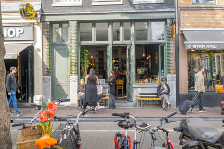 Amsterdam-Netherlands - August 21 2017; Customers being waited on on city street outside cafe as others pass with cycles in foreground.のeditorial素材