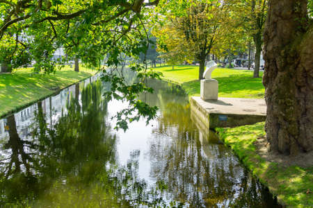 Rotterdam Netherlands - August 23 2017;  Small white public art sculpture on bank of leafy shady Westersingel canal in city.の写真素材
