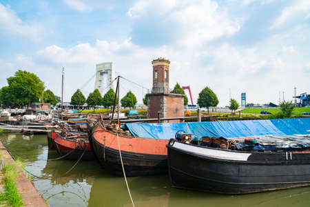 Rotterdam Netherlands - August 22 2021; Old traditional boats moored along bank of Old Harbour with historic brick turret structure and bridge in background..のeditorial素材