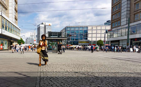 Berlin, Germany - August 28 2017; People in street, Alexanderplatz, wide cobbled pedestrian area in city, one modern woman walking with ice cream and mobile  phone.のeditorial素材