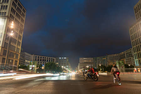 Berlin, Germany - August 28 2017; Lighting and effects of night in city, streets and buildings with long exposure light trails from passing vehicles and blurred cyclist and motorcyclist in motion on road.のeditorial素材