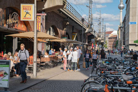 Berlin Germany - August 26 2017;Narrow lane in city with cafes and people including group four young men in white tops with caps on backwardsのeditorial素材