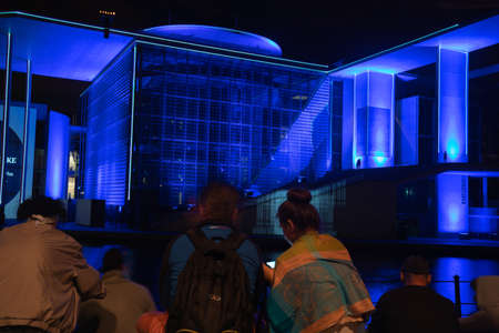 Berlin, Germany - August 28 2017; Blue  light effects of buildings beyond tourists  in foreground sitting looking across  in Government District Berlinのeditorial素材