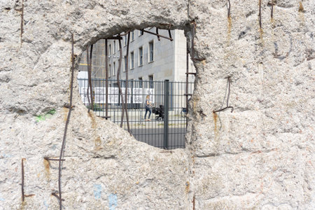 Berlin, Germany - September 25, 2017: Scene through Berlin Wall hole broken with reinforcing iron view out onto street where woman pushes pram past.のeditorial素材