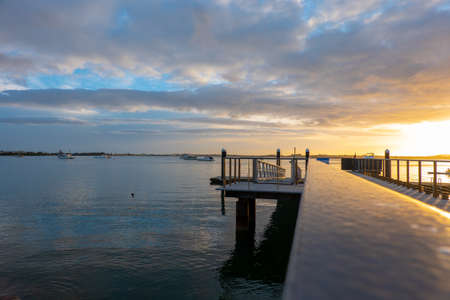 Tauranga waterfront pier and railing reflecting golden glow of morning sunrise, on edge of harbor, New Zealand.の写真素材