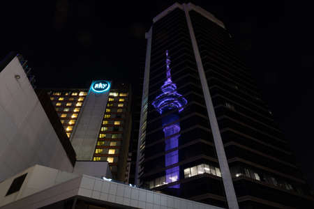 Auckland new zealand - December 25 2021; NIght scene tall circular tower illuminated blue reflected in glass facade of surrounding building.のeditorial素材
