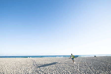 Mount Maunganui New Zealand- January 2 2022; Single paddle-boarder carries board and paddle over sand to water casting long shadow in morning light.のeditorial素材