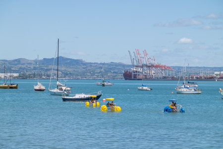 Tauranga New Zealand - January 17 2022; Beach-goers enjoying summer day on waterfront and in water at Pilot Bay with port background.のeditorial素材