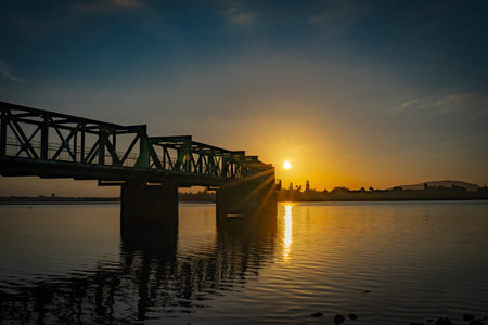 Long curving lines of railway bridge in silhouette as sunrises over horizon and span.