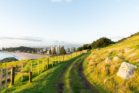 Track around Mount Maunganui along fence-line with view out to buildings in town and ocean beach,...