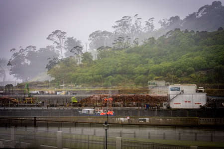 Gisborne New Zealand - February 7 2022; Raining day at working port with fishing boat at wharf logs stacked for export and equipment in zoom blur giving effect of impressionist industrial movement.against backdrop of Kaiti Hill.のeditorial素材