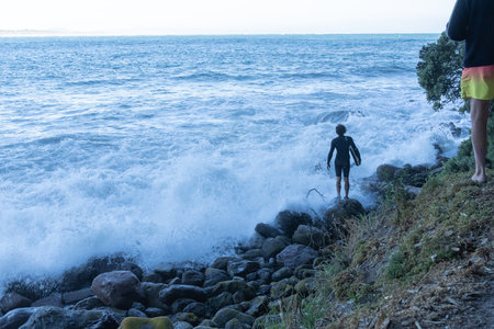 Tauranga New Zealand - January 01 2022; Young male stands on rugged rocky sea edge with wave board deciding when to risk jumping in.のeditorial素材