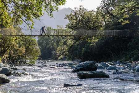 Hollyford Valley New Zealand - April 15 2022; Tramper on crossing one at time,river using swing-bridgeのeditorial素材