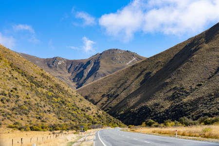 Road through folds of tussock and broom clad mountain ridges Lindis Pass, South Canterbury New Zealand.の写真素材
