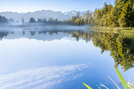 Perfect reflection in Lake Matheson surrounded by beautiful natural forest under blue sky with view to Southern Alps and Mount Cook, South Island new Zealand.の写真素材