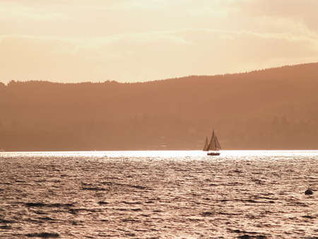 Silhouette distant hills and yacht sailing in under red sky at sunset on Lake Taupo, New Zealand.の写真素材