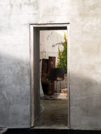 View through opening on concrete wall into courtyard with rusty old barbeque cooker and green ivy on wall.の写真素材