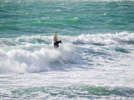 Raglan, New Zealand -June 7 2008 Lone surfer coming off as surfboard points vertically out riding...