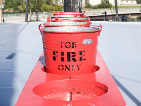 Row of red buckets in rack with sign for fire only for emergency.の写真素材