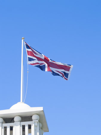 Union Jack fluttering in breeze from pole on turret against blue sky.の写真素材