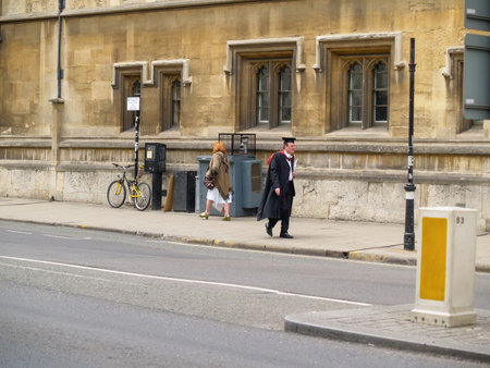 Oxford United Kingdom - June 19 2009; University city street scene with man in gown and mortarboard or Oxford cap walking on sidewalk.のeditorial素材