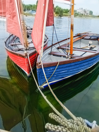 Two sailing dinghies with red sails moored to jetty on reservoir in United Kingdom.