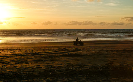 Beach in silhouette as sunsets on distant horizon over ocean.の写真素材