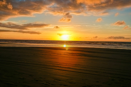 Dramatic dark sky over Beach in silhouette as sunsets on distant horizon over ocean.の写真素材