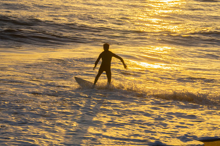 Back-lit and unrecognizable surfer in golden glow of evening light at Castlecliff Beach, Wanganui.