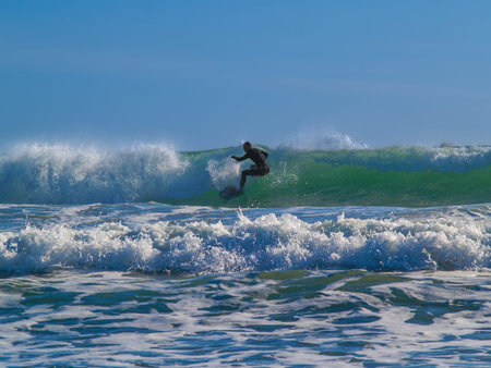 Surfer in silhouette in curl of wave under blue sky as sun comes up.
