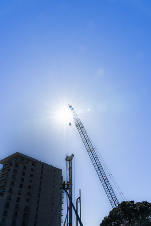 Construction crane topped by sun star-burst over building site.の写真素材