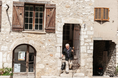 Saint Paul de Vence, Provence,  France - May 2 2011; Senior man and small dog leaving front doorway of old stone apartment.のeditorial素材