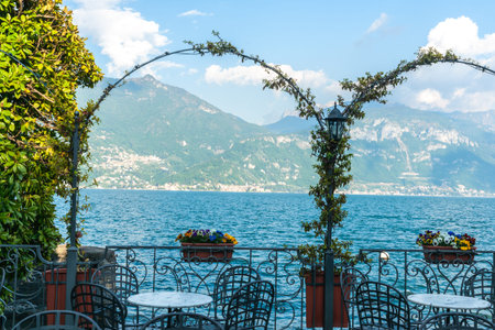 Sun on mountain side across Lake Como through vines over arches on lake edge Menaggio, Italy on shores of Lake Como.の写真素材