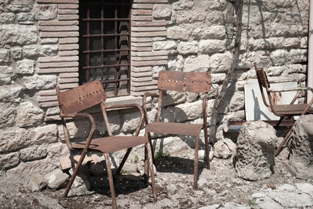 Two old rusty chairs outside stone wall in street scen in old Italian town.の写真素材