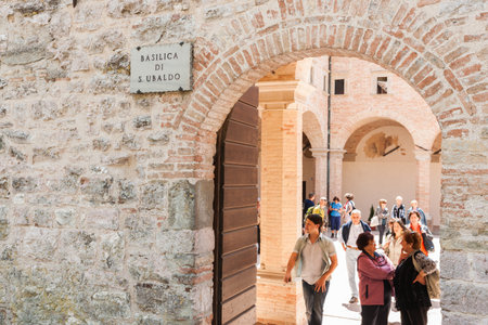 Gubio Umbria, Italy, May 12 2011; Name plate on wall at entrance as tourists wander in courtyard of medieval basilica of Saint Ubaldo.のeditorial素材