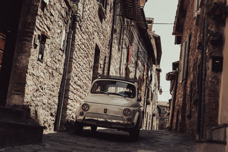 Gubbio Italy - May 12 2011; Vintage small Italian car parked in narrow old town street between stone walls old style image.のeditorial素材