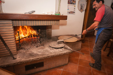 Umbria, Italy, May 25 2011; Baker lifts shovel of hot embers to put on top of cooked pizza to finish traditional process.のeditorial素材