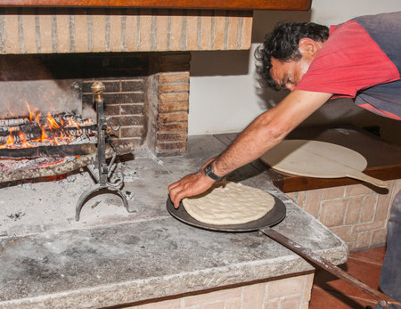 Umbria, Italy, May 14 2011; Baker placing Traditional Italian pizza in open fireplace for cooking.のeditorial素材