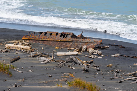 Old wrecked hulk of washed-up boat rusty and surrounded by driftwood in Patea Coastal South Taranaki , New Zealand.の写真素材