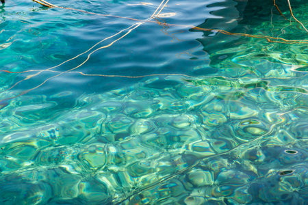 Patterned clear water surface and bottom of bay with boat ropes crossing.の写真素材