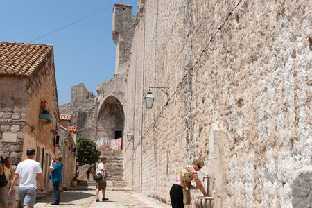 Dubrovnik Croatia - May 28 2011; People walk along path and woman washed hands in font inside wall of medieval city high wall leads to steps and peopleのeditorial素材