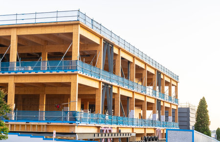 Multi-level wooden and steel framed building under construction with blue mesh and scaffolding edge...