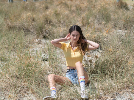 Teenage girl sitting in grass at beach at Mount Maunganui New Zealand.の写真素材