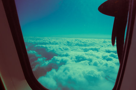 Nostalgic effect ofpPlane propellor and white puffy cloud under blue sky through plane window while flying above cloud.の写真素材