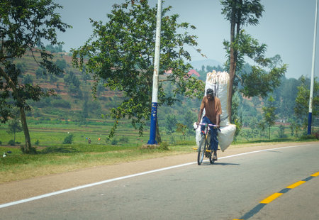Rwanda -September 4 2025; African man riding bicycle loaded with large white sacks of plastic transporting it to destination.の写真素材