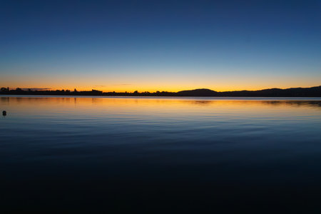 Blue of sky and water separated by orange and red of sunrise over Waimapu Harbour.の写真素材