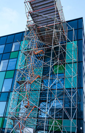 Green glass exterior of office building rising skyward with scaffolding erected to provide for...